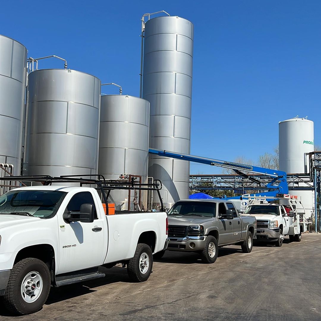 Service trucks parked beside tall stainless process tanks